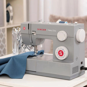 Singer Heavy Duty 4452 sewing machine sitting with blue fabric under the presser foot on a white table.